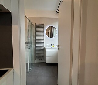 Moderní koupelna s dlažbou, sprchovým koutem a kulatým zrcadlem, vybavená žebříkovým radiátorem, tvoří elegantní a funkční prostor.