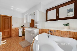 Prostorná koupelna s dlažbou, rohovou vanou a dřevěnými okny, moderní vybavení a světlé tóny dodávají místnosti čistý a elegantní vzhled.
