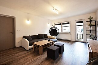 Světlý obývací pokoj s parketovou podlahou, velkými okny a moderním nábytkem, ideální pro pohodlné bydlení v rekonstruovaném stylu.