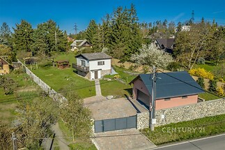 Rodinný dům s velkou zahradou, obklopený stromy. Dlažba v příjezdové cestě, moderní půdorys, klidná lokalita poblíž přírody.