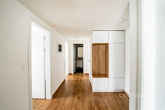 Chodba s parketovou podlahou, moderní vestavěné skříně a světlé bílé stěny, vedoucí k elegantní koupelně v rekonstruovaném bytě.