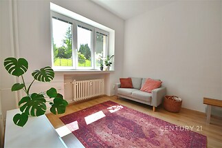 Světlý obývací pokoj s velkými okny, parketovou podlahou a moderním designem, ideální pro rodinné bydlení v klidné lokalitě.