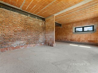 Nezařízený obývací pokoj, odhalené cihlové zdi, betonová podlaha, moderní styl, velké okno poskytující přirozené světlo.