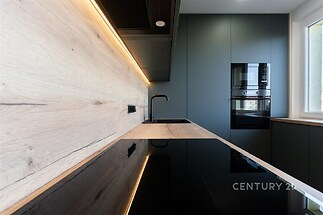 Moderní kuchyň s dřevěnou pracovní plochou, vestavěnými spotřebiči a LED osvětlením vytváří elegantní a funkční prostor.