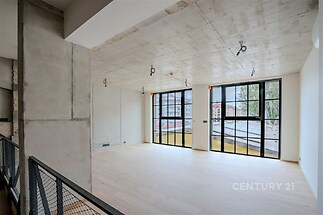 Světlý obývací pokoj s velkými okny, betonovým stropem a dřevěnou podlahou nabízí moderní a industriální atmosféru.