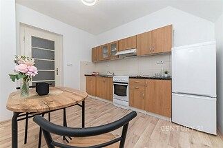 Kompaktní kuchyň s parketovou podlahou, moderními dřevěnými skříňkami a světlým interiérem, ideální pro menší bytový prostor.