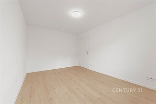 Světlý pokoj s parketovou podlahou, čisté bílé stěny, moderní svítidlo na stropě, minimalistický styl, připraven k nastěhování.