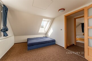 Podkrovní ložnice s kobercovou podlahou, velkým střešním oknem a moderním osvětlením, ideální pro světlý a útulný prostor.