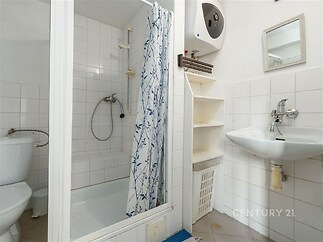 Koupelna s dlažbou a sprchovým koutem, vybavená umyvadlem a toaletou. Neutrální barvy a funkční uspořádání vytvářejí praktický prostor.