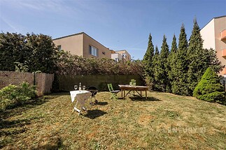 Udržovaná zahrada s prostorným travnatým povrchem, obklopená živým plotem. Slunečný venkovní prostor vhodný pro relaxaci a grilování.