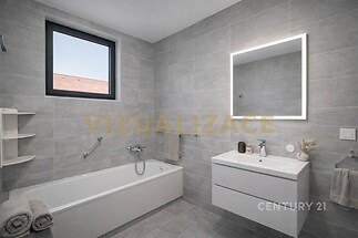 Moderní koupelna s šedou dlažbou, prostornou vanou a vestavěným umyvadlem. Velké zrcadlo s osvětlením, světlý a elegantní design.