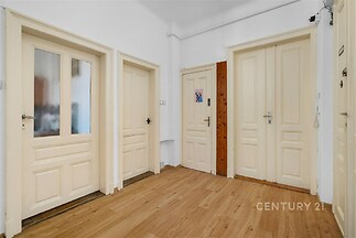 Chodba s parketovou podlahou, světlými dveřmi a bílými stěnami nabízí příjemné přirozené osvětlení, vhodná pro moderní zařízení.