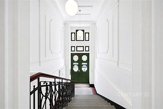 Světlé vstupní schodiště s elegantním zábradlím a dlažbou, vysoké stropy, původní dekorativní omítka, prostorný interiér.