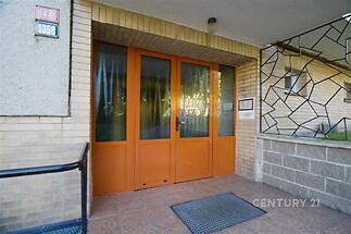 Vstupní prostor s keramickou dlažbou, moderními skleněnými dveřmi a cihlovými stěnami.