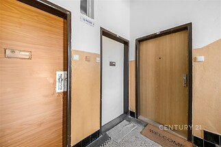 Vstupní chodba s betonovou podlahou, dřevěnými dveřmi a světlými stěnami v bytové budově