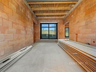 Nezařízený obývací pokoj s velkými okny a surovou stěrkou; cihlové zdi, nedokončená podlaha, přírodní světlo