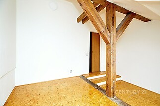 Podkrovní místnost se světlou dřevěnou podlahou, viditelnými trámovými prvky a bílými stěnami, ideální pro rekonstrukci nebo modernizaci.