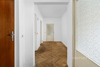 Široká vstupní hala s parketovou podlahou, bílými stěnami a moderním designem, nabízí přístup do dalších místností a vyzařuje prostornost.