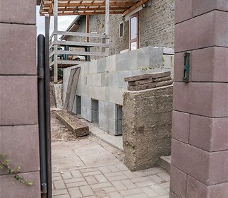 Venkovní rekonstrukce domu s betonovým základem a novou terasou, cihlová dlažba, částečně dokončený vzhled, vhodné pro úpravy