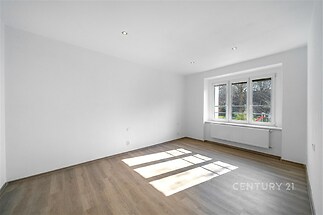 Světlý obývací pokoj s parketovou podlahou a velkými okny, moderní styl, nově rekonstruovaný prostor s výhledem do zahrady.