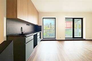 Moderní kuchyň s parketovou podlahou a velkými okny, která nabízí dostatek přirozeného světla, elegantní dřevěné skříně a moderní černý interiér