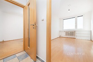 Světlá místnost s laminátovou podlahou a velkými okny, která nabízí moderní výhled. Vedlejší prostor s dřevěnými dveřmi a neutrální dlažbou.