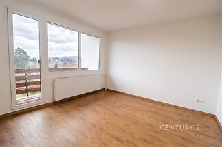 Světlý obývací pokoj s parketovou podlahou, velká okna s výhledem a moderní bílá výmalba, ideální pro rekonstrukci či úpravy podle vlastních představ