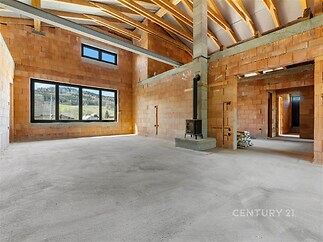 Otevřený obývací pokoj s velkými okny, betonová podlaha a krbová kamna, dodávají prostoru moderní a průmyslový styl.