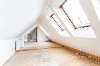 Podkrovní prostor s dřevěnou podlahou, velkými střešními okny a bílými stěnami, světlý interiér, ideální pro rekonstrukci.