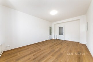 Světlý obývací pokoj s moderní parketovou podlahou a velkými okny, čerstvě renovovaný s čistými bílými stěnami.