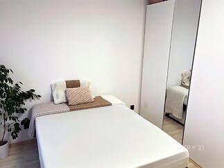 Světlá ložnice s parketovou podlahou, vestavěnými skříněmi a moderním minimalistickým designem, ideální pro útulné bydlení.