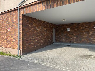 Krytý parkovací prostor s cihlovými zdmi, dlažba na podlaze a moderní osvětlení.