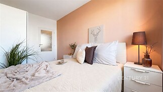 Světlá ložnice s moderním designem, světle oranžovou stěnou, vestavěnou skříní a útulnou atmosférou, ideální pro relaxaci.