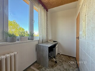 Malá pracovně zařízená místnost s moderní dlažbou, psacím stolem a velkým oknem, které poskytuje přirozené světlo a výhled ven.