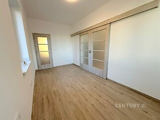 Prostorná ložnice s dřevěnou podlahou, moderní posuvné dveře a světlé stěny vytvářejí pocit vzdušnosti a elegance.