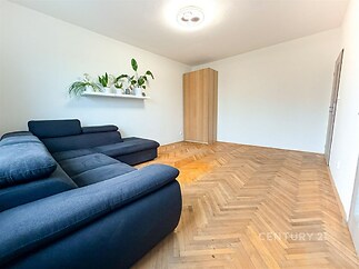 Světlý obývací pokoj s parketovou podlahou, moderní sedačkou a vestavěnou skříní, minimalistický interiér s dekorativními rostlinami.