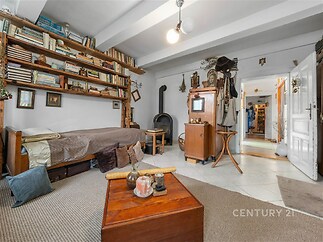 Útulný obývací pokoj s dlažbou a krbovými kamny, dřevěné poličky plné knih, rustikální dekorace, světlé stěny a částečně koberec