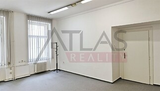 Světlá místnost s velkými okny, kobercovou podlahou a bílými stěnami, vhodná pro kancelářské využití, ve velmi dobrém stavu.