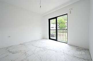 Světlý pokoj s velkými okny a balkónovými dveřmi, moderní dlažba, bílé stěny, výhled do zahrady, novostavba