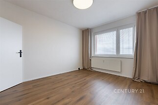 Prázdný pokoj s parketovou podlahou, velkým oknem a moderní výzdobou, ideální pro vytvoření světlého obytného prostoru