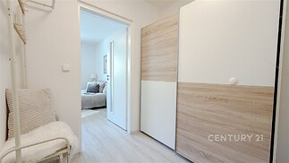 Předsíň s dřevěnou vestavěnou skříní, světlé dřevěné podlahy, moderní vzhled, dveře vedoucí do světlé ložnice