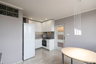 Moderní kuchyň s dlažbou, vestavěnými skříněmi a světlým nábytkem, elegantní design a velká okna přináší dostatek přirozeného světla.