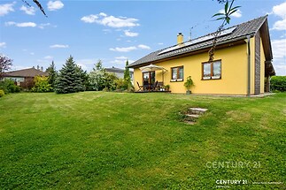 Zahrada s terasou, prostorný rodinný dům, udržovaný trávník, klidná lokalita, moderní fasáda, venkovní posezení.