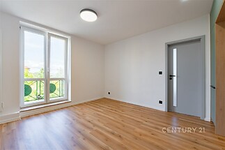 Světlý obývací pokoj s parketovou podlahou, velká okna poskytují dostatek denního světla, moderní design s neutrálními barvami.