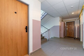 Chodba v bytovém domě s dlažbou a dřevěnými dveřmi, dobře udržovaný prostor se světlými stěnami a moderními liniemi poskytuje čistý vzhled.
