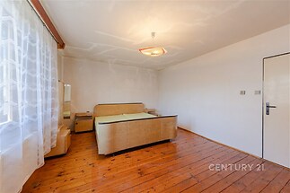Prostorná ložnice s dřevěnou podlahou, velkým oknem a světlým interiérem, ideální pro moderní design a útulnou atmosféru.