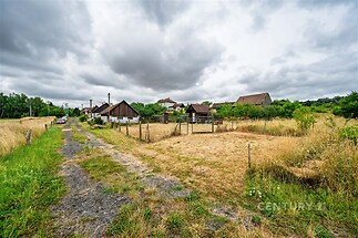 Polní cesta lemovaná travnatými plochami a staršími stodolami na venkově, ideální místo pro klidné bydlení nebo farmářský život.