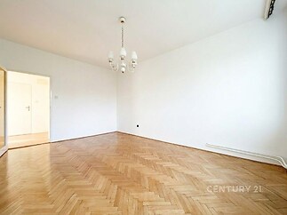 Světlý obývací pokoj s parketovou podlahou, jednoduchou bílou stěnou a klasickým lustrem, ideální pro moderní interiérový design.