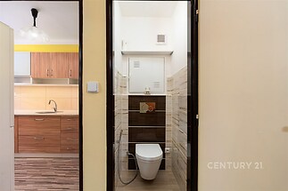 Malá koupelna s moderní dlažbou, závěsným WC a světlým keramickým obkladem, harmonicky ladí s okolní retro kuchyní s dřevěnými prvky.