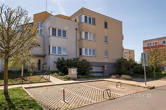 Moderní bytový dům s parkováním, minimalistická architektura, čisté linie, světlé fasády, vstup do garáže, udržovaná předzahrádka.